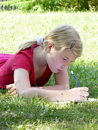 Mädchen schreibt im Gras.